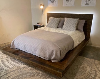 May include: A modern platform bed with a dark wood finish. The bed features a headboard with integrated lighting and is dressed with a white comforter, a gray quilt, and decorative pillows. The bed frame measures approximately 78 inches long.