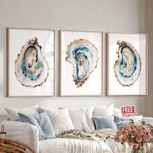 May include: Three watercolor paintings of oyster shells. Each painting features a different oyster shell with a blue, green, and brown color scheme. The paintings are framed and displayed on a white wall.