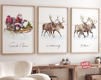 Könnte beinhalten: Drei Aquarelle in Holzrahmen, die den Weihnachtsmann in einem von Rentieren gezogenen Schlitten zeigen. Das erste Bild zeigt den Weihnachtsmann im Schlitten, das zweite zeigt die Rentiere, die den Schlitten ziehen, und das dritte zeigt die Rentiere, die durch den Schnee laufen. Der Text "Santa Claus is coming to town!" steht unter den Bildern.