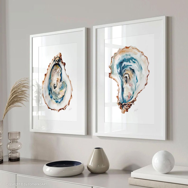 Puede incluir: Dos impresiones enmarcadas en acuarela de conchas de ostra. La obra de arte presenta tonos de azul, marr&oacute;n y blanco, con detalles intrincados. Las impresiones se exhiben en marcos blancos, agregando un toque de elegancia al arte de tem&aacute;tica costera.