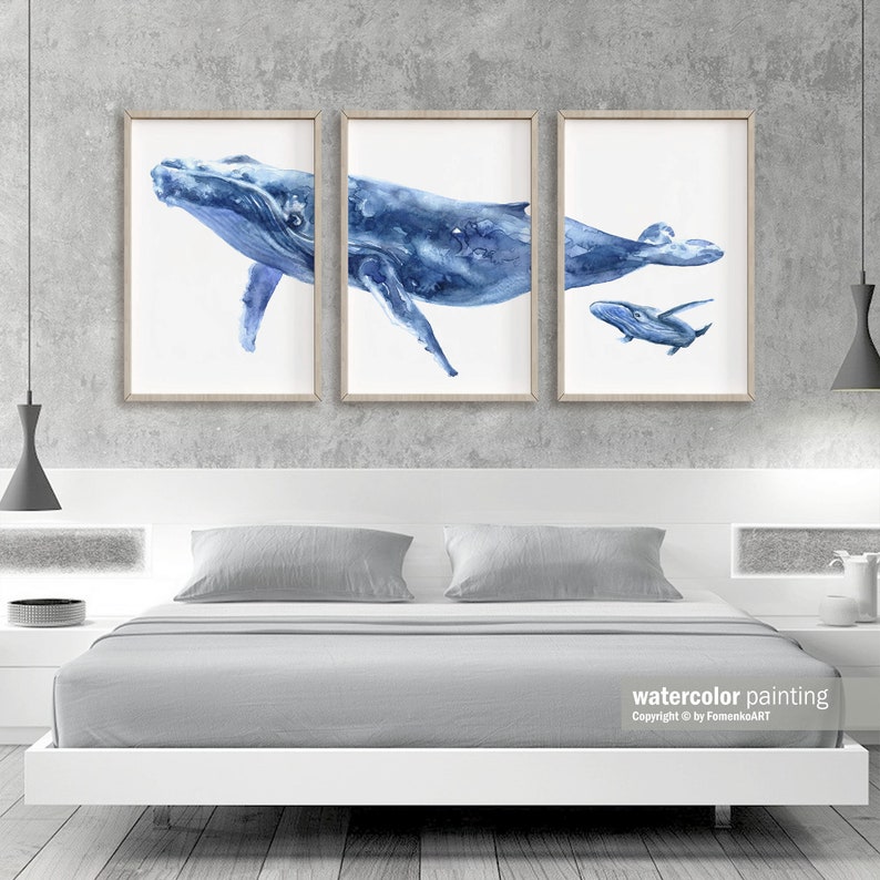 May include: Three framed watercolor paintings of whales in shades of blue. The artwork depicts a large whale, a whale with a calf, and a whale swimming. The frames are a light wood color. The text "watercolor painting" is visible in the bottom right corner.
