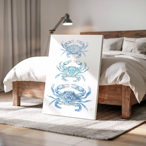 May include: A vertical canvas art print featuring three watercolor crabs in shades of blue. The crabs are arranged one above the other against a white background. The artwork is displayed in a bedroom setting, leaning against a bed.