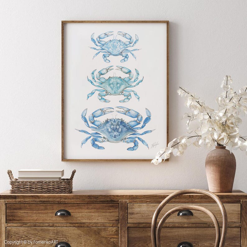 May include: A framed print featuring three blue crab illustrations. The crabs are depicted in a watercolor style, with varying shades of blue and intricate details. The artwork is displayed in a wooden frame, suitable for coastal or nautical decor.