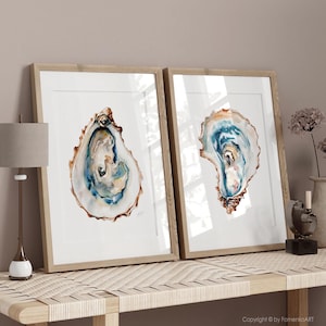 Puede incluir: Dos impresiones enmarcadas en acuarela de conchas de ostra. La obra de arte presenta tonos de azul, marr&oacute;n y blanco, con una representaci&oacute;n detallada del interior de la concha. Los marcos son de madera clara y el arte se exhibe sobre una superficie clara.