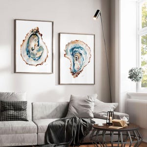 Puede incluir: Dos impresiones enmarcadas de acuarela de conchas de ostra. La obra de arte presenta tonos de azul, marr&oacute;n y blanco, con detalles intrincados. Los marcos son de color marr&oacute;n neutro y las impresiones se exhiben en una pared blanca.