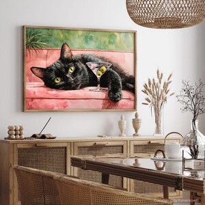 May include: A framed watercolour painting of a black cat relaxing on a pink sofa, with a martini glass containing olives. The cat has yellow eyes. The background has green and pink hues.