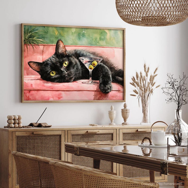 May include: A framed watercolour painting of a black cat relaxing on a pink sofa, with a martini glass containing olives. The cat has yellow eyes. The background has green and pink hues.