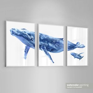 May include: A set of three watercolor paintings depicting a mother whale and her calf swimming in the ocean. The paintings are framed in white and feature a light blue background.