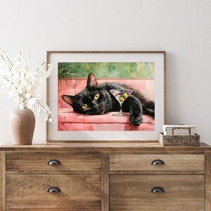 May include: Watercolour painting of a black cat reclining on a pink sofa, with a martini glass containing olives. The cat has yellow eyes and is looking at the viewer. The artwork is framed in a wooden frame.