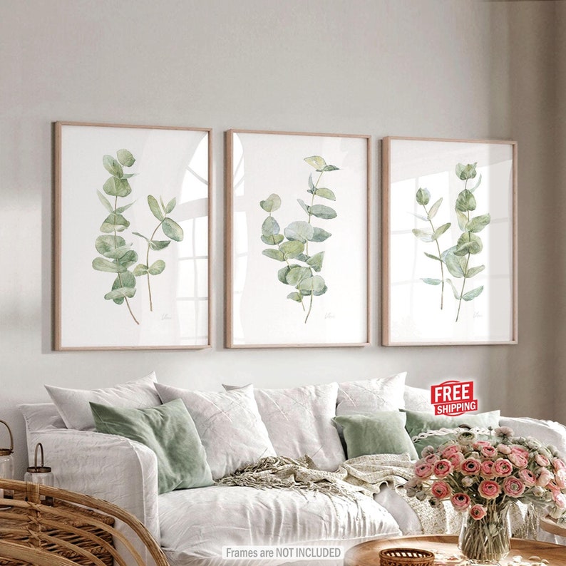 Puede incluir: Conjunto de tres impresiones de acuarela enmarcadas con hojas de eucalipto verdes sobre un fondo blanco. Las impresiones est&aacute;n en marcos de madera simples y est&aacute;n colgadas en una pared blanca sobre un sof&aacute; blanco.