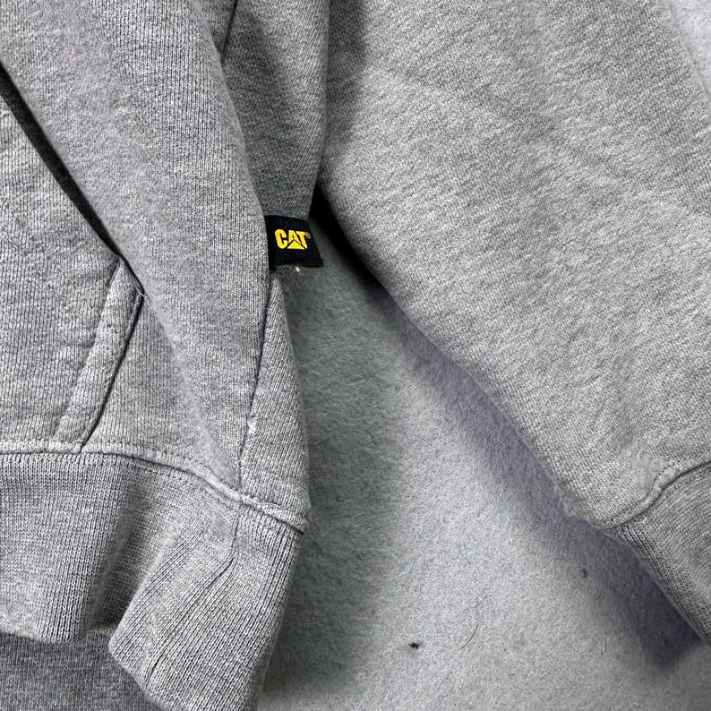 May include: A set of three ceramic mugs with a speckled, matte finish. The mugs are in shades of cream, light gray, and dark gray. Each mug has a simple, minimalist design and a rounded handle. The mugs are stacked on top of each other.