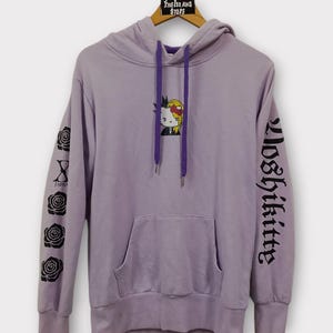Pu&ograve; includere: Una felpa con cappuccio lavanda con una tasca frontale e un cappuccio con coulisse viola. La felpa con cappuccio presenta una grafica a cartoni animati e il testo "Yoshikitty" sulla manica destra. La manica sinistra ha un disegno di rose e la parola "Japan".