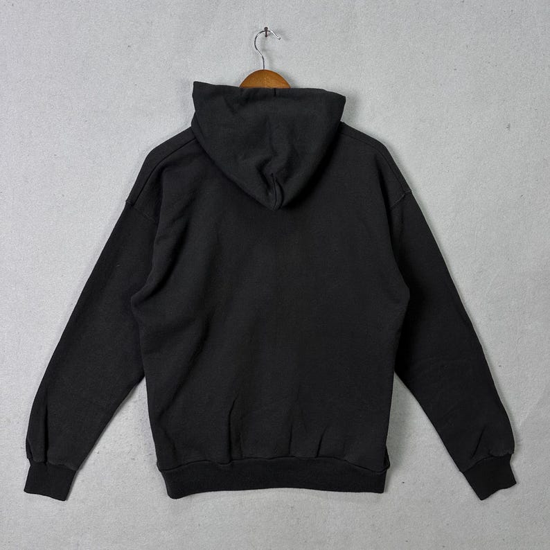May include: A black hooded sweatshirt with long sleeves, suspended from a wooden hanger. The sweatshirt features a hood and ribbed cuffs and hem. The garment is made of a soft, comfortable material.