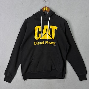 May include: Black hoodie with a kangaroo pocket and white drawstring. The front displays the yellow "CAT" logo and "Diesel Power" text.