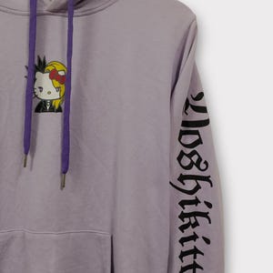Pu&ograve; includere: Felpa con cappuccio color lavanda con una grafica di Hello Kitty in stile punk. La felpa ha un cappuccio con coulisse, una tasca frontale e la scritta "Loser Kitty" stampata in nero sulla manica.