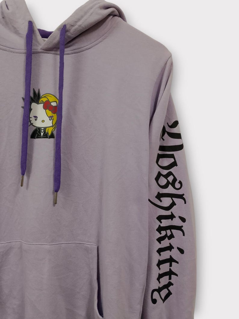Pu&ograve; includere: Felpa con cappuccio color lavanda con una grafica di Hello Kitty in stile punk. La felpa ha un cappuccio con coulisse, una tasca frontale e la scritta "Loser Kitty" stampata in nero sulla manica.