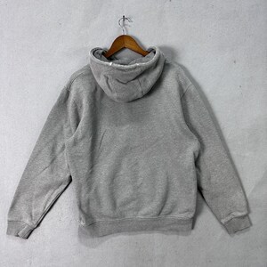 May include: A gray hoodie with a drawstring hood, long sleeves, and a kangaroo pocket. The sweatshirt is hanging on a wooden hanger against a light gray background. The back of the hoodie is visible.