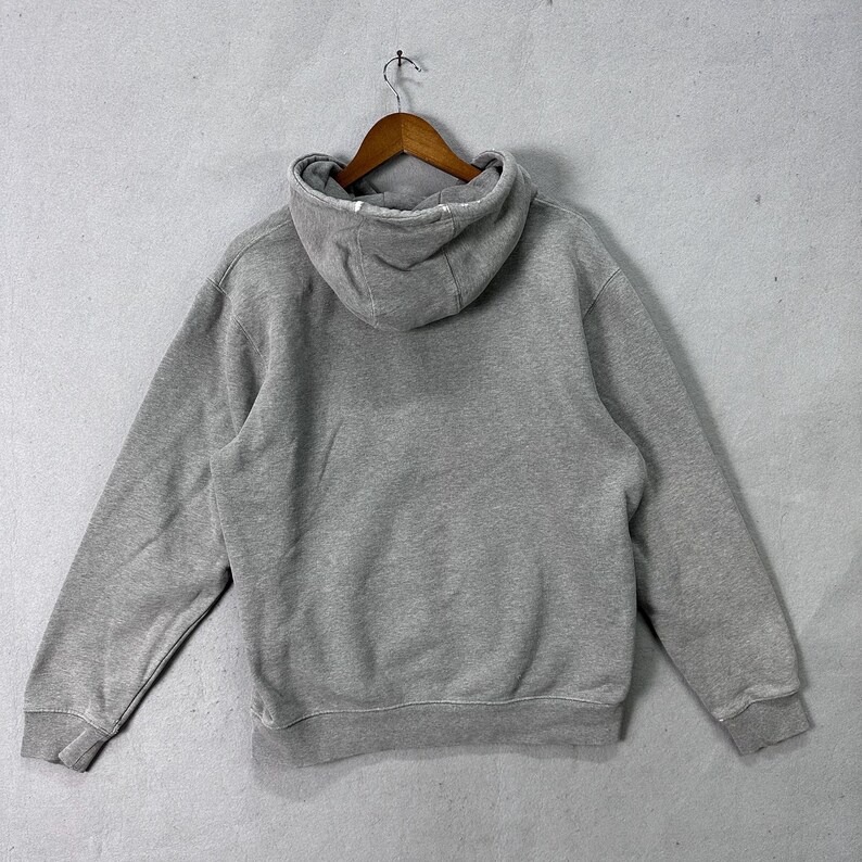 May include: A gray hoodie with a drawstring hood, long sleeves, and a kangaroo pocket. The sweatshirt is hanging on a wooden hanger against a light gray background. The back of the hoodie is visible.