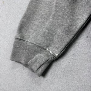 May include: Close-up of a gray sweatshirt sleeve, showing the ribbed cuff and a portion of the arm. The fabric appears to be a soft, knit material. The cuff has a seam with visible stitching.