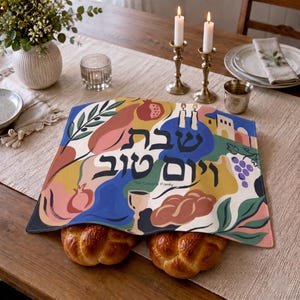 Könnte beinhalten: Eine rechteckige Challah-Abdeckung aus Stoff mit einer bunten abstrakten Illustration von Granatäpfeln, Weintrauben, einem Kiddusch-Becher und zwei geflochtenen Broten. Der hebräische Text lautet Schabbat Schalom, darunter steht The Cohen Family.