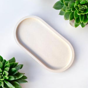 Peut inclure: Un plateau ovale blanc en béton ou en céramique. Le plateau est lisse et a une surface légèrement texturée.