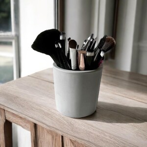Peut inclure: Un porte-pinceaux de maquillage en béton gris avec une variété de pinceaux de maquillage noirs et argentés à l'intérieur.