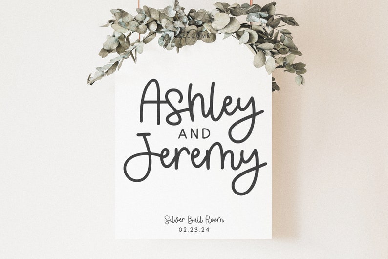 Peut inclure: Une pancarte blanche avec une calligraphie noire qui dit "Ashley et Jeremy" avec le texte "Silver Ball Room 02.23.24" en dessous. La pancarte est suspendue &agrave; une guirlande de feuilles d'eucalyptus.