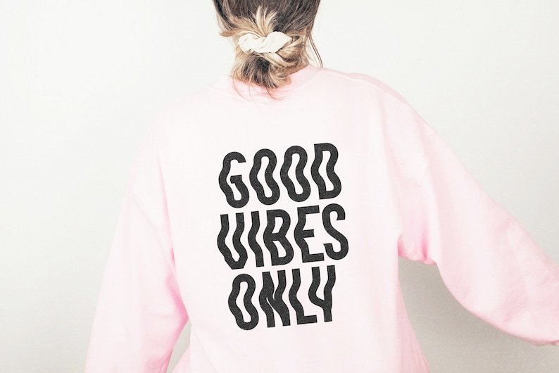 Op de afbeelding: Roze sweatshirt met de tekst "GOOD VIBES ONLY" in het zwart gedrukt op de achterkant.