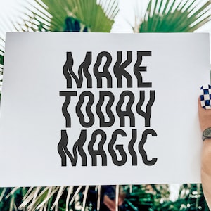 Op de afbeelding: Witte kaart met zwarte tekst die "MAKE TODAY MAGIC" zegt, vastgehouden door een hand met zwart-wit geblokte nagellak.