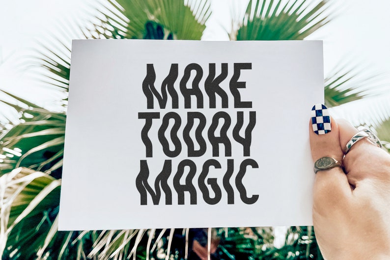 Op de afbeelding: Witte kaart met zwarte tekst die "MAKE TODAY MAGIC" zegt, vastgehouden door een hand met zwart-wit geblokte nagellak.