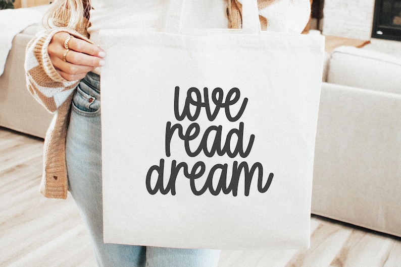 Op de afbeelding: Witte tote bag met zwarte tekst die "love read dream" zegt.