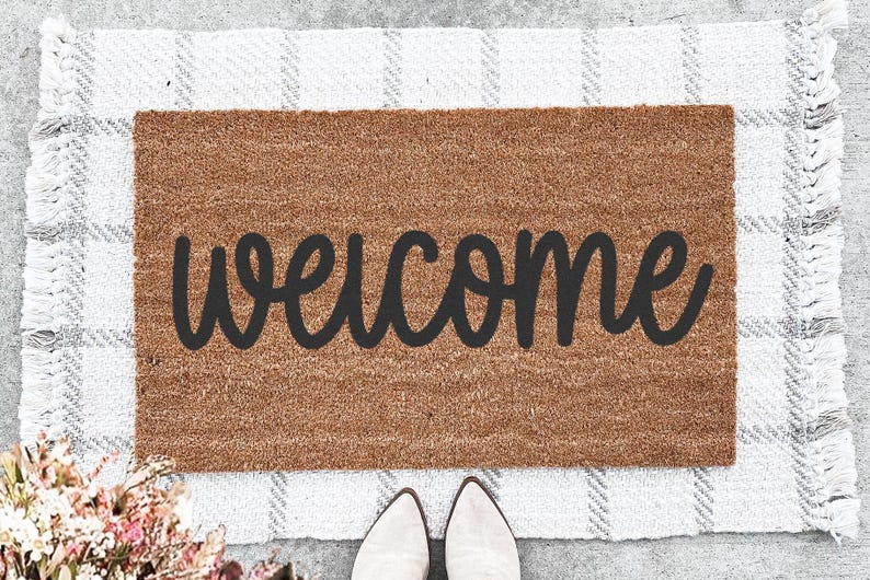 Op de afbeelding: Een bruine kokosmat met het woord "welcome" in zwarte cursieve letters.