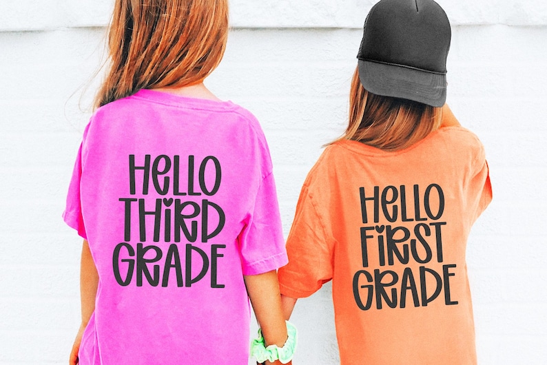 May include: Two children wearing pink and orange t-shirts with the text "HELLO THIRD GRADE" and "HELLO FIRST GRADE" in black. One child wears a black cap. The children are holding hands.