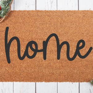 Peut inclure: Un paillasson en fibre de coco brun avec le mot "home" &eacute;crit en cursive noire.