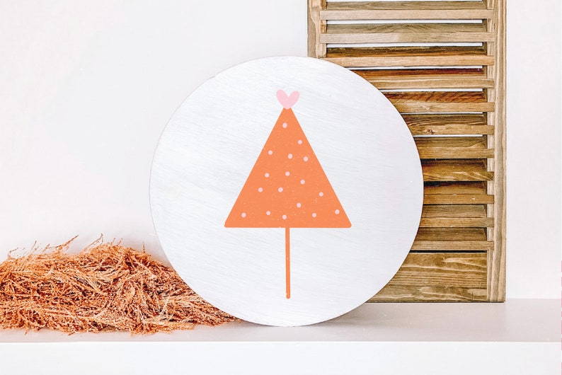 May include: A white round wooden sign with an orange triangle with white polka dots and a pink heart on top. The triangle has a thin white stem.