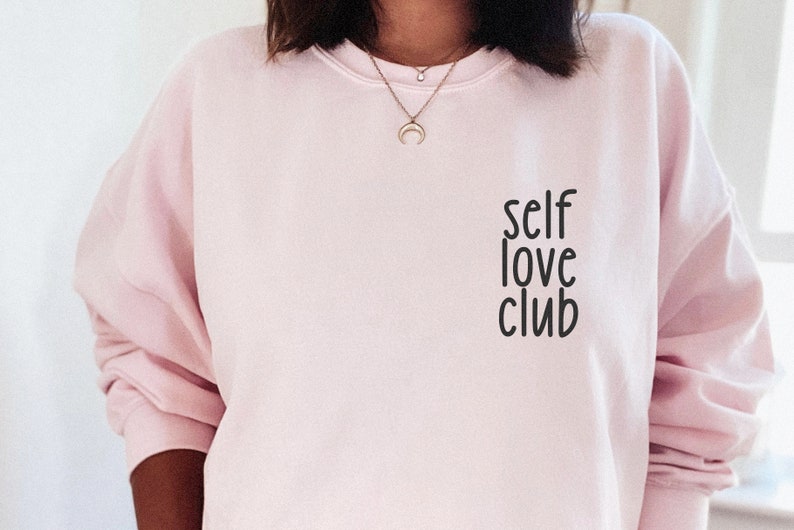 K&ouml;nnte beinhalten: Ein rosa Sweatshirt mit dem Aufdruck "self love club" auf der Vorderseite.