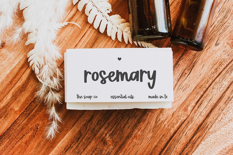 May include: A white bar of soap with the text "rosemary" in black script font. The soap is labeled "the soap co", "essential oils", and "made in tx".