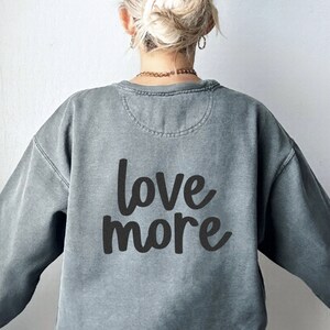 May include: A gray sweatshirt with the text "love more" printed on the back in black.