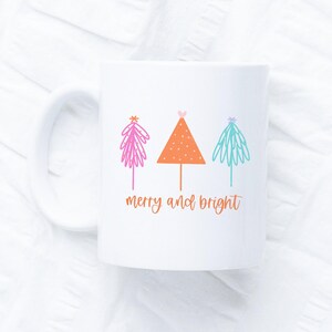 May include: White ceramic mug with a Christmas tree design in pink, orange, and blue. The mug has the text "merry and bright" in orange.