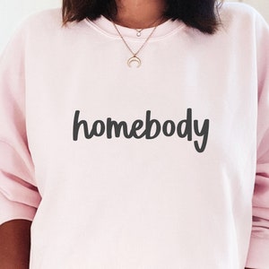 May include: A pink sweatshirt with the word "homebody" written in black cursive lettering.
