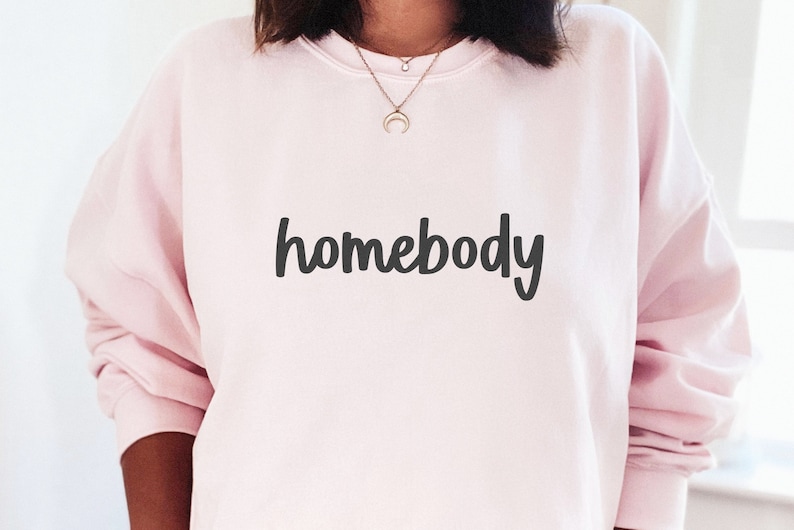 May include: A pink sweatshirt with the word "homebody" written in black cursive lettering.