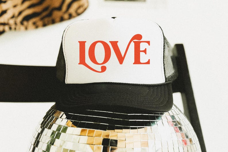 May include: A black and white trucker hat with the word "LOVE" in red script across the front. The hat is resting on a disco ball. The hat has a white front panel and a black mesh back.