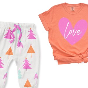 May include: A two-piece pajama set for children featuring a pink heart with the word "Love" on a coral t-shirt and white pants with a pink, orange, and blue tree pattern.