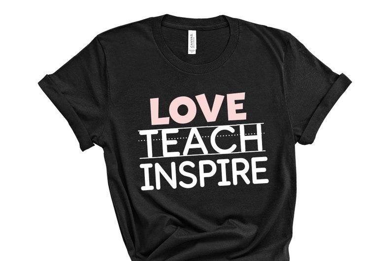 Op de afbeelding: Zwart T-shirt met de tekst "LOVE TEACH INSPIRE" in witte en roze letters.