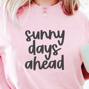 May include: A pink t-shirt with the text "sunny days ahead" in black lettering.