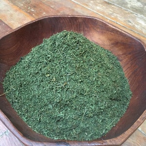 May include: A wooden bowl filled with a large amount of dried, finely chopped green herbs.