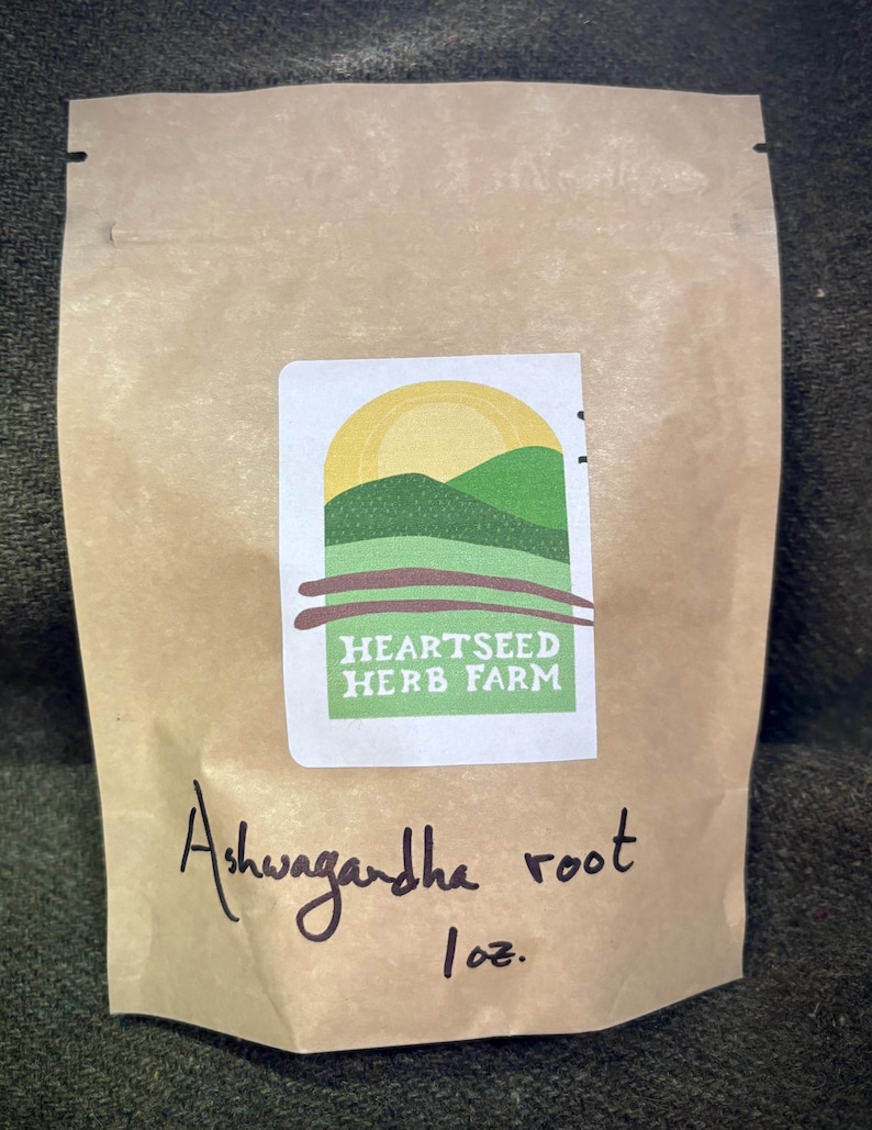 Puede incluir: Una bolsa de papel marr&oacute;n con una etiqueta blanca que dice "Heartseed Herb Farm" y un logotipo verde y amarillo. La bolsa est&aacute; etiquetada "Ashwagandha root 1 oz."