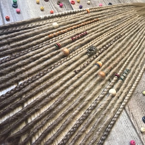 May include: A set of 20 brown and blonde ombre synthetic dreadlocks with various beads and charms. The dreadlocks are arranged in rows on a wooden surface.