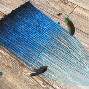 Puede incluir: Un conjunto de rastas sintéticas ombre azul y negro. Las rastas están dispuestas en forma de abanico sobre una superficie de madera.