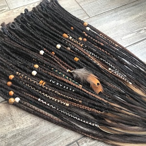 May include: A set of brown and blonde synthetic dreadlocks with beads and a feather accent. The dreadlocks are arranged in a fan shape and have a variety of textures and colours.